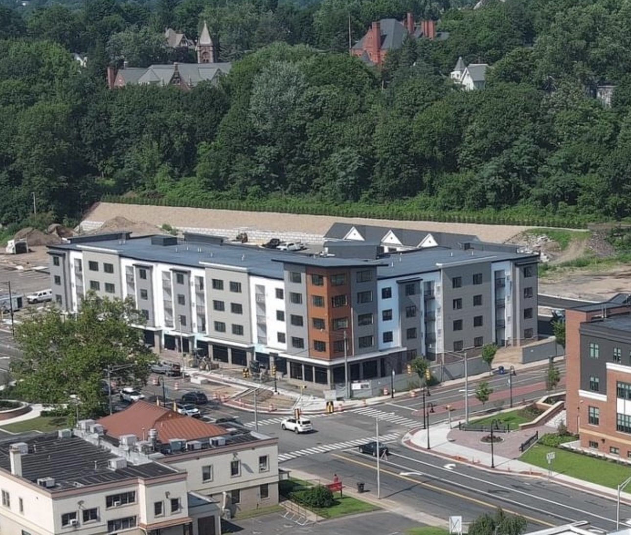 aerial view of a four-story multifamily building located on a street corner in front of a cluster of trees