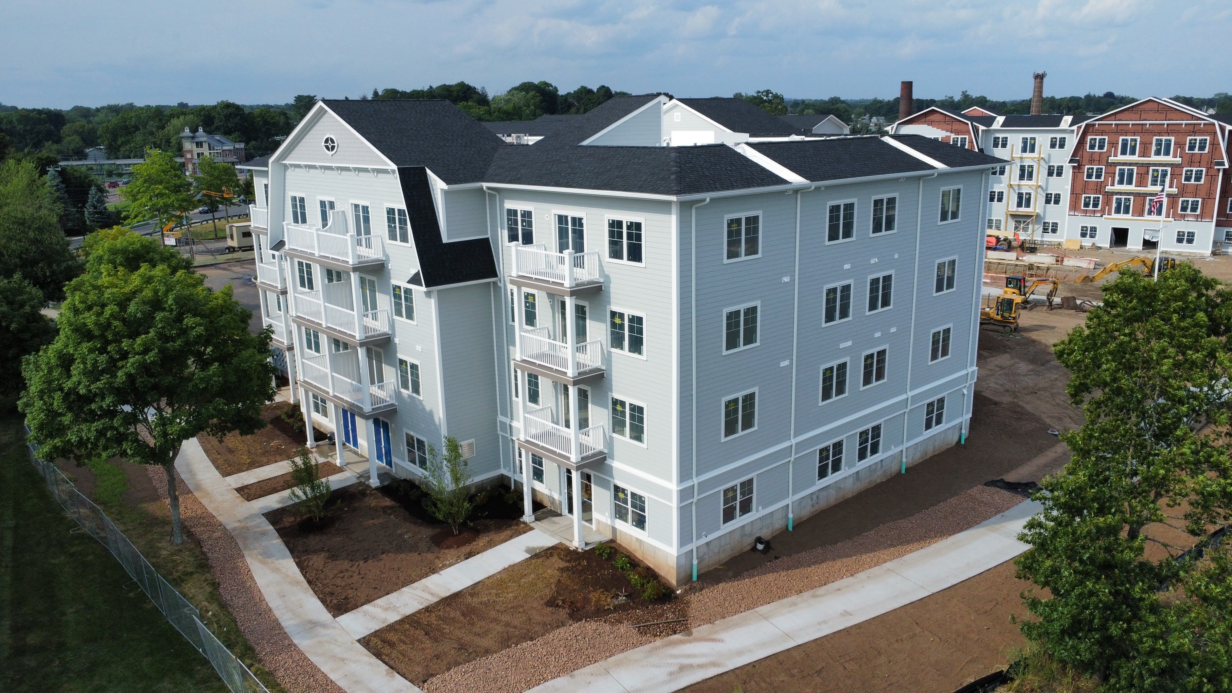 aerial view of a recently built light blue four-story multifamily building with other multistory buildings under construction in the background